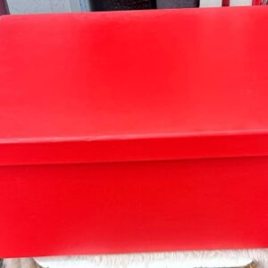 Caja roja grande con tapa cerrada sobre una superficie, fondo con estantes desenfocados.