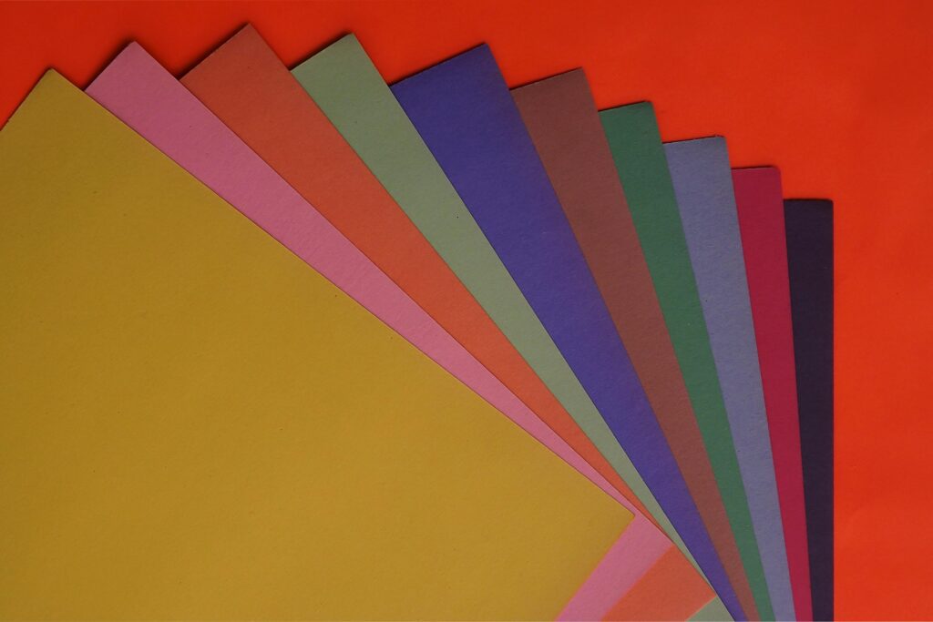 A vibrant flat lay of assorted colored papers on a red surface, great for creative projects.