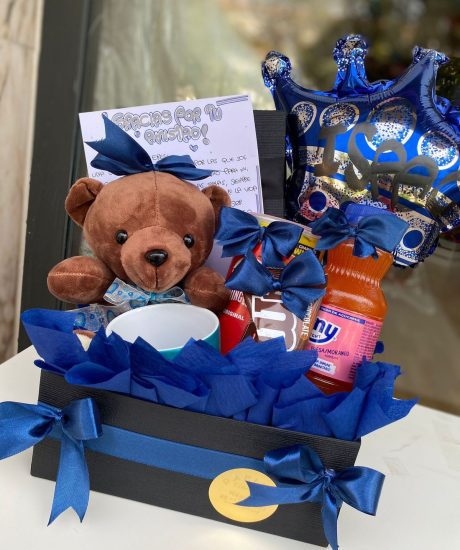 Cesta azul para hombre con taza personalizada, galletas, peluche azul y globo de corona negra. Un detalle con estilo y dulzura desde Madrid.